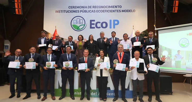Grupo de funcionarios en dos filas sosteniendo certificados de reconocimiento como 'Modelo EcoIP'. La imagen captura el momento de la distinción otorgada por el Ministerio del Ambiente (MINAM) al Fondo MIVIVIENDA por su gestión de prácticas ecoeficientes